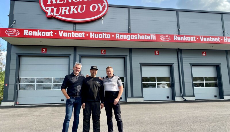 Tre glada män framför en bilverkstad