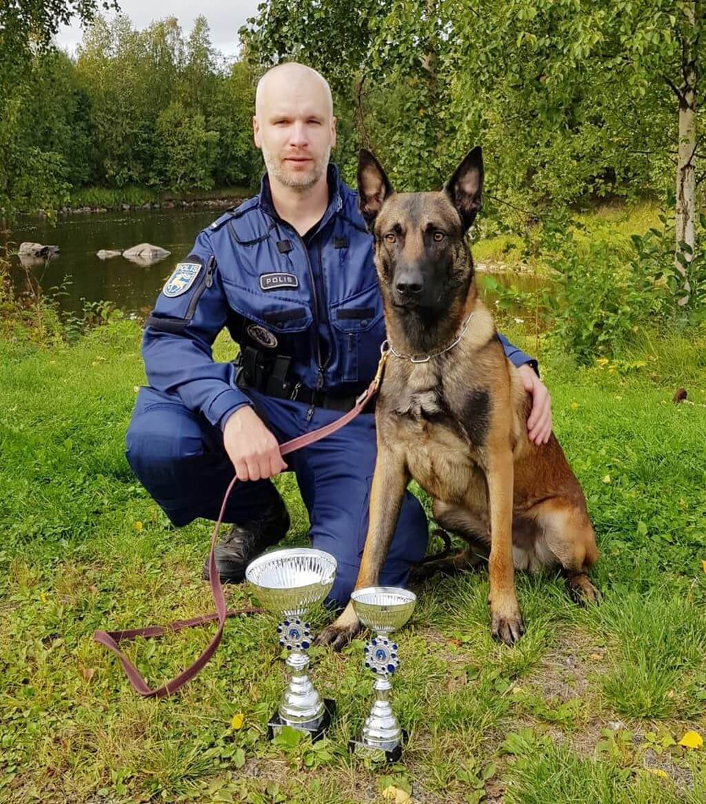 Polis på huk bredvid en schäfer. Framför dem två prispokaler