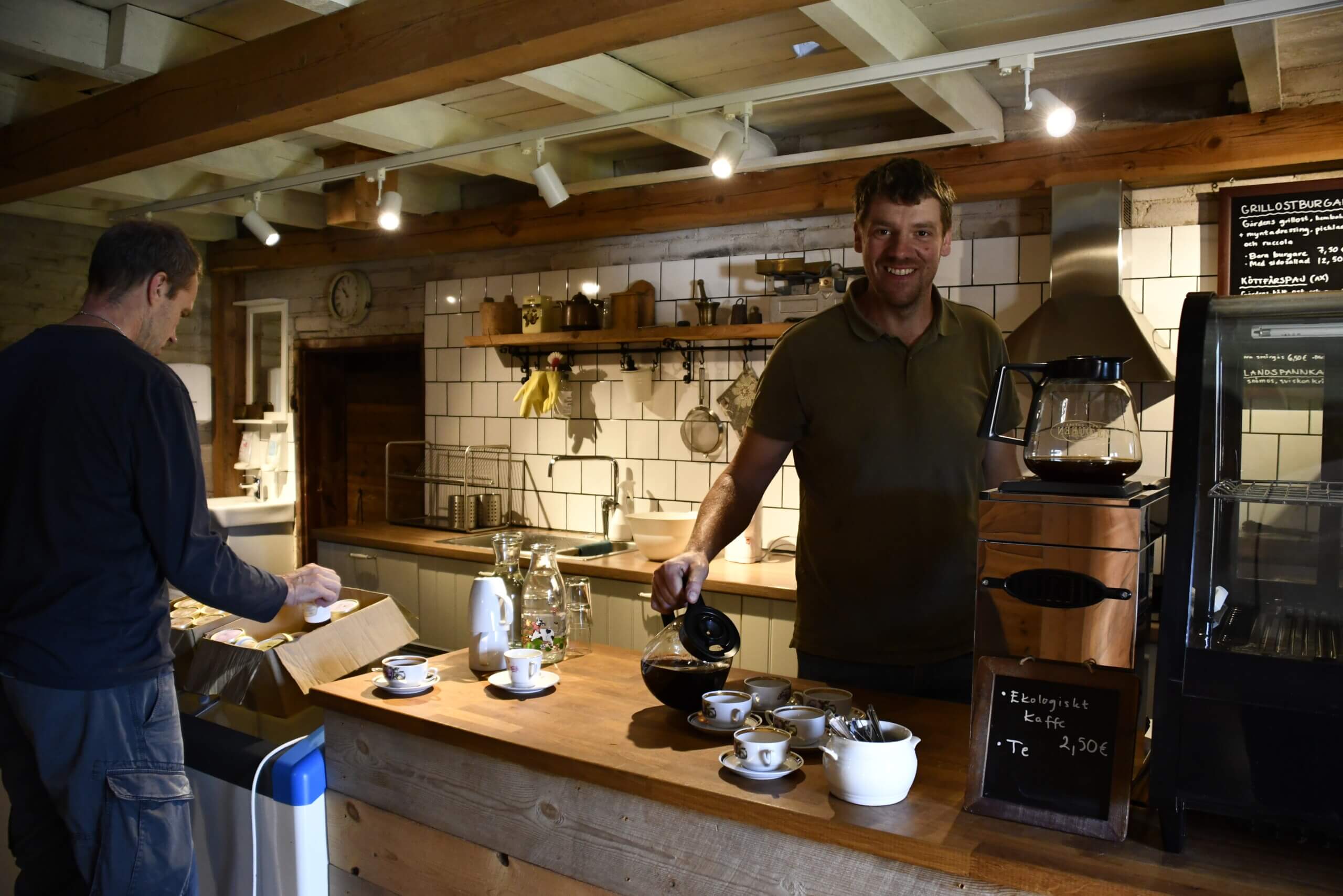Leende man står bakom försäljningsdisk och häller upp kaffe i en kopp