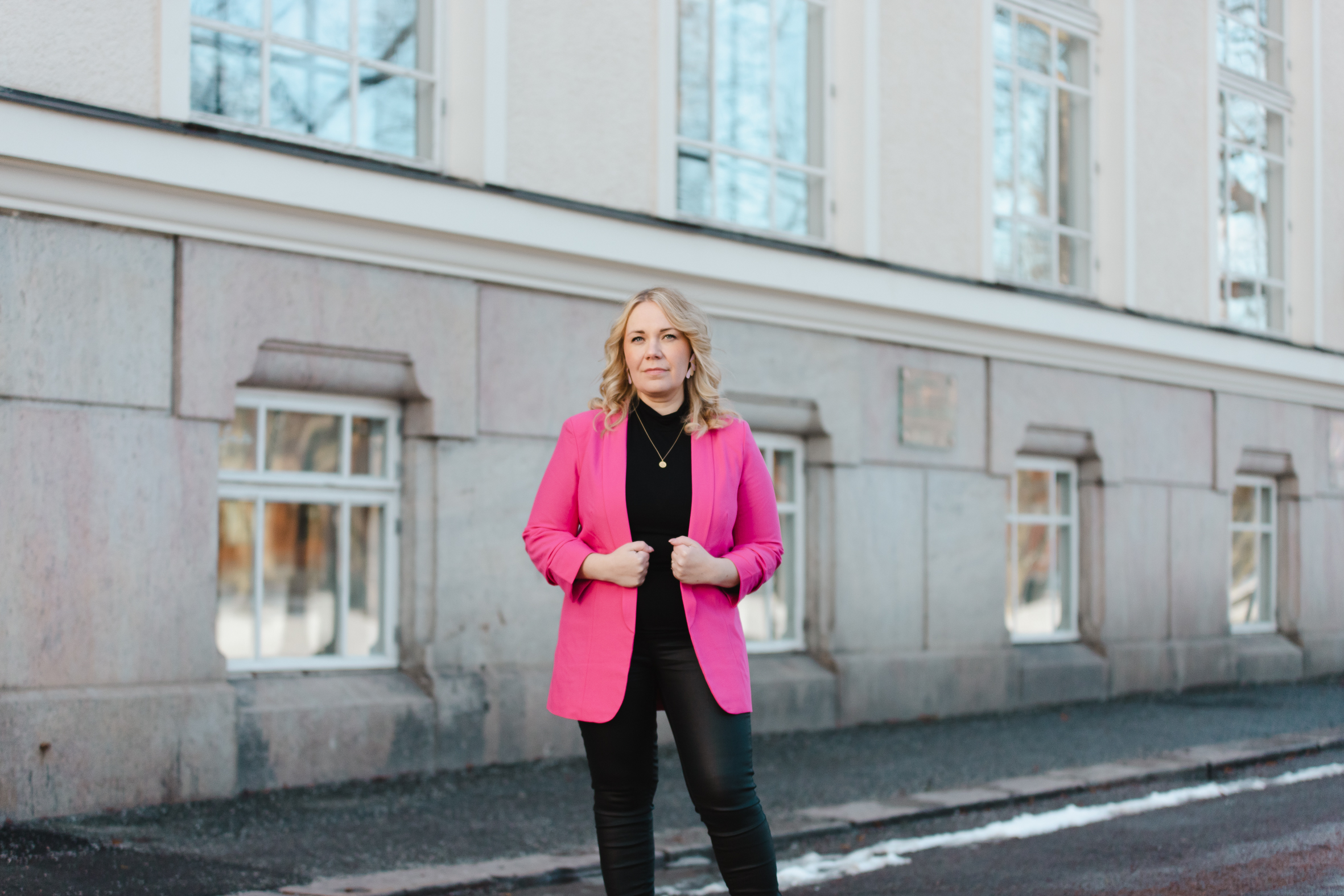 kvinna med rosa kavaj framför stort hus