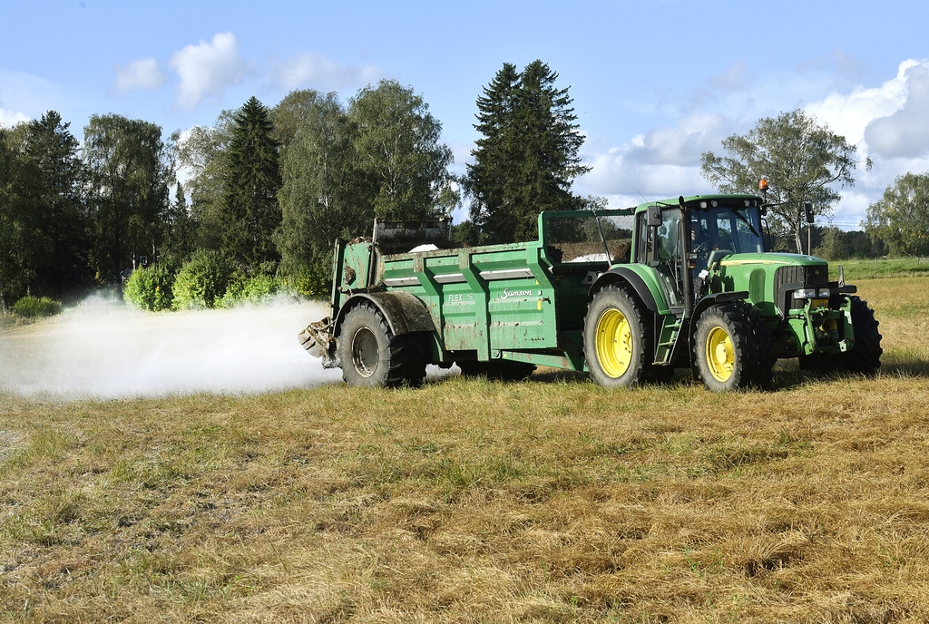 Traktor med släp sprider gips på åker