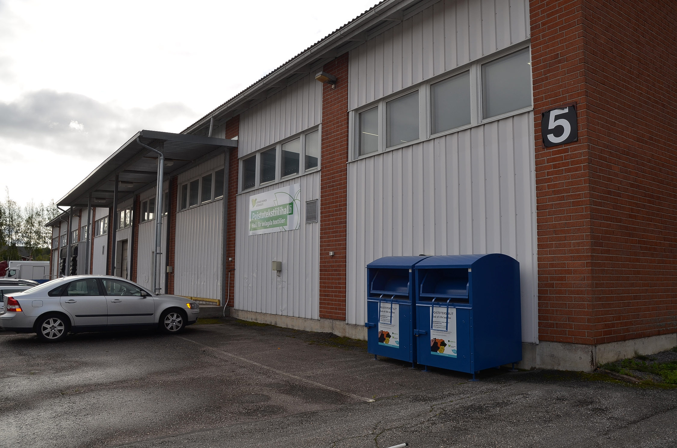 en industribyggnad med blåa insamlingskärl framför