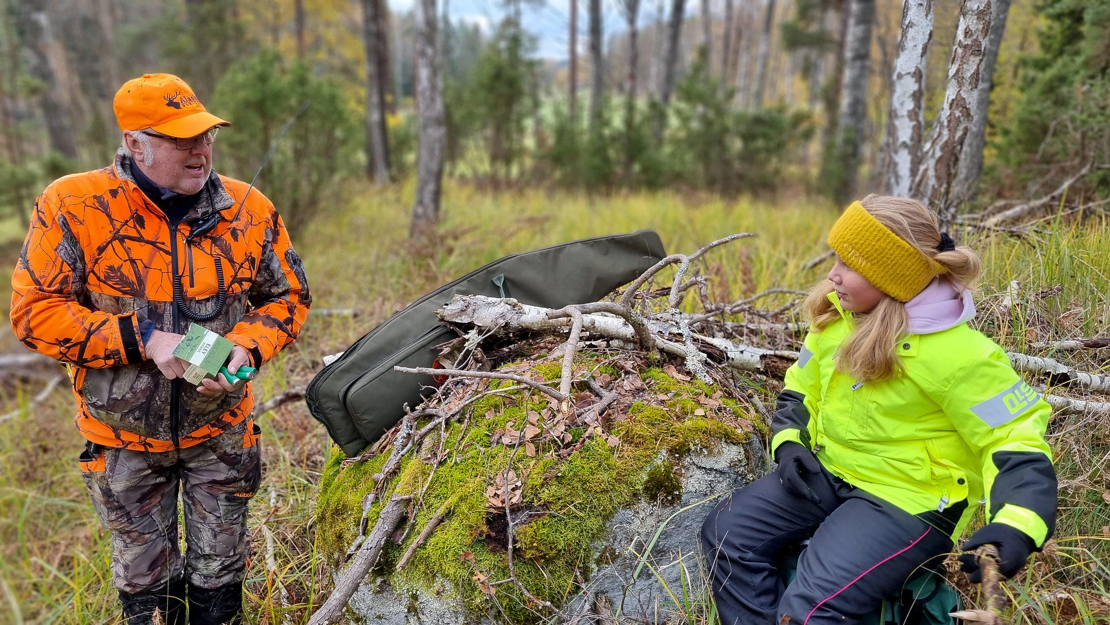 Jägare och flicka samtalar vid sten.