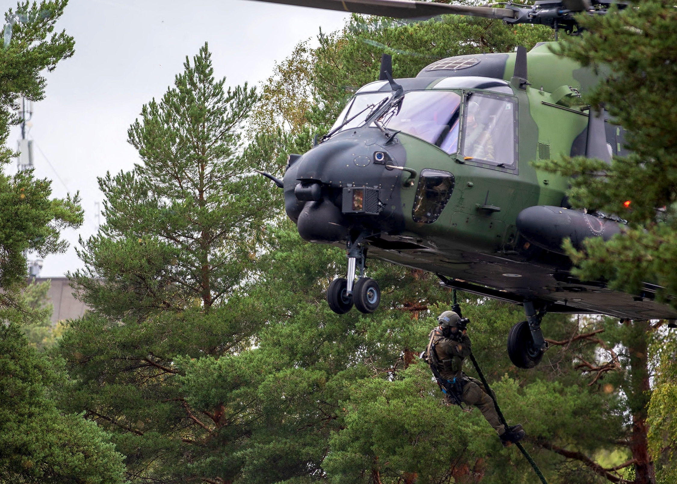 Kamouflagefärgas helikopter sänker ner man i skogen.