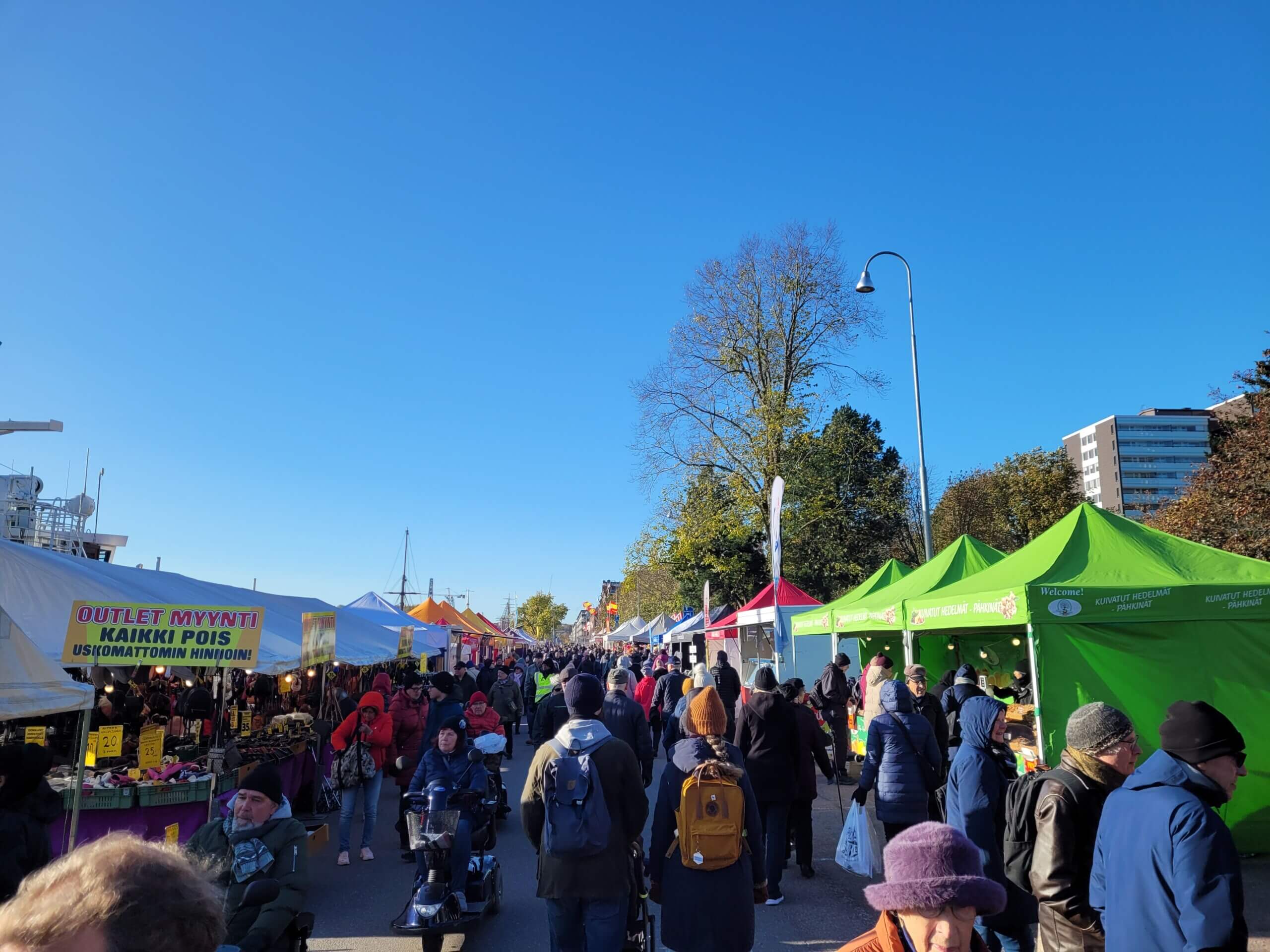 Folkvimmel på marknad i soligt väder.