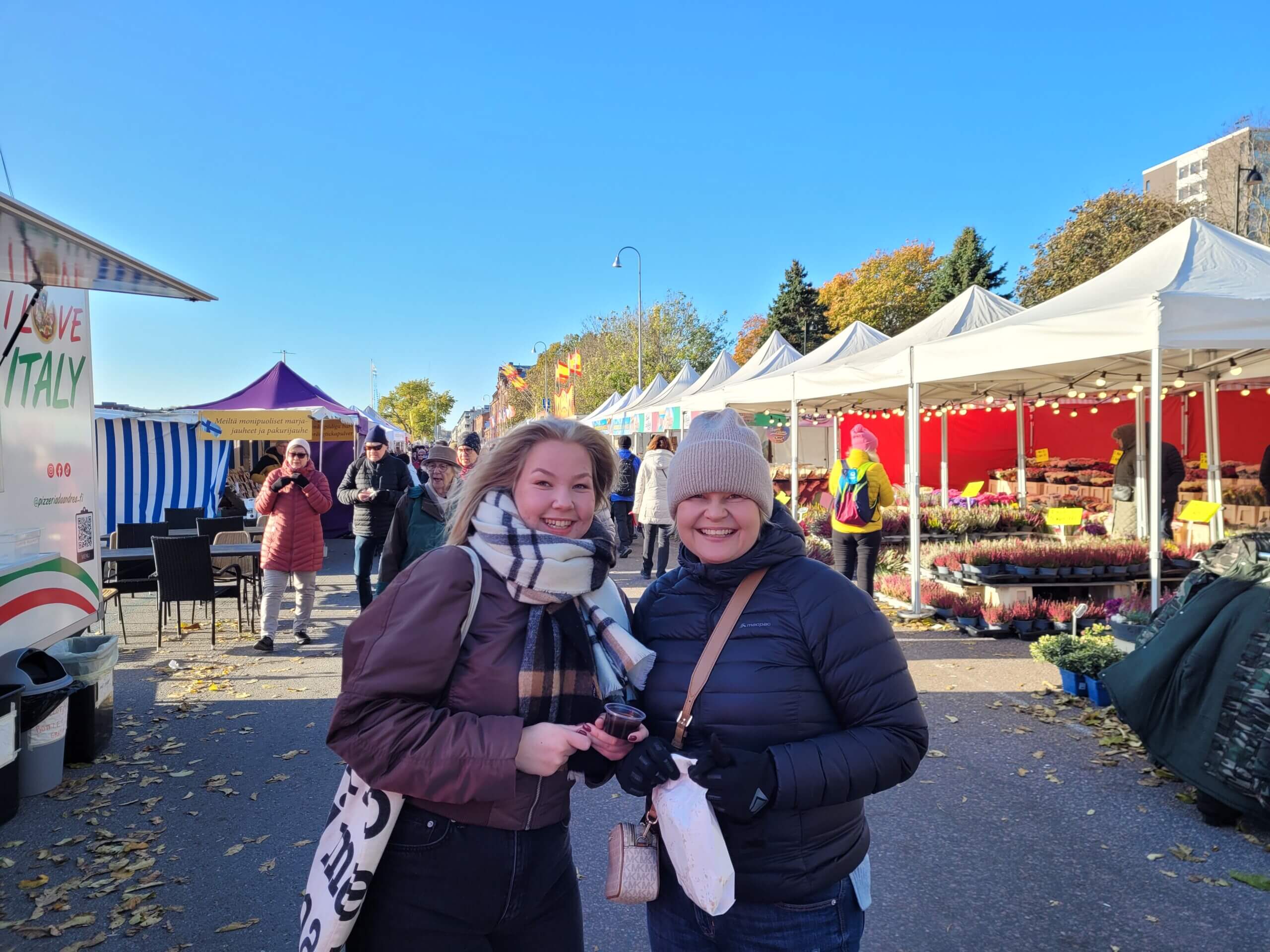 En ung kvinna och hennes mamma ler glatt mot kameran med en påse churros i handen.