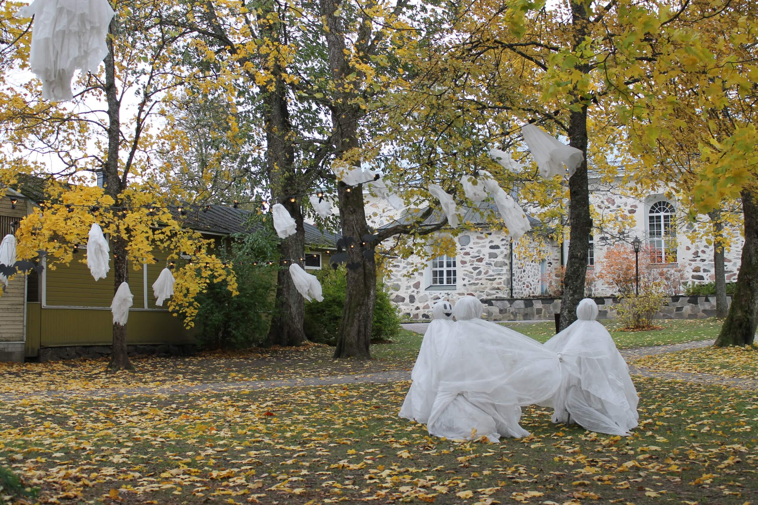 Halloweendekorationer utomhus, utanför Ekenäs kyrka. Spöken som dansar i ring och mindre spöken och fladdermöss hänger från träden.
