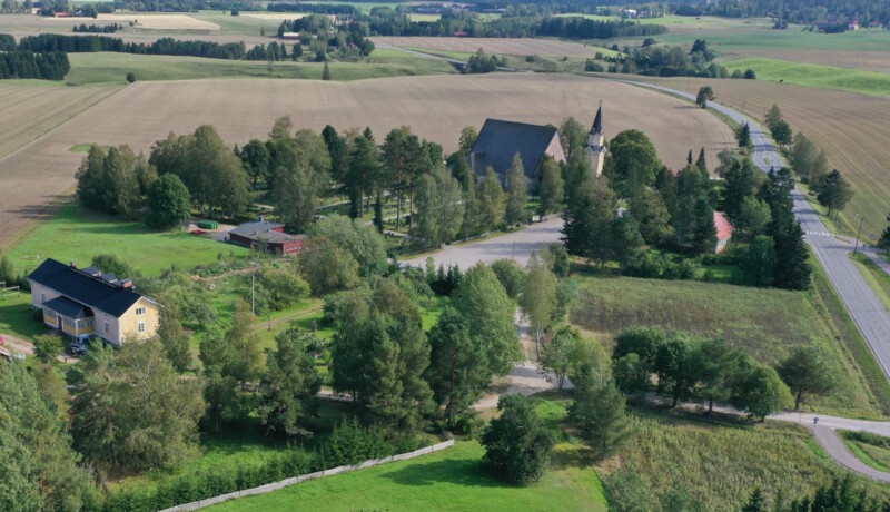 Landskapsvy över gles bosättning, en stenkyrka och åkrar