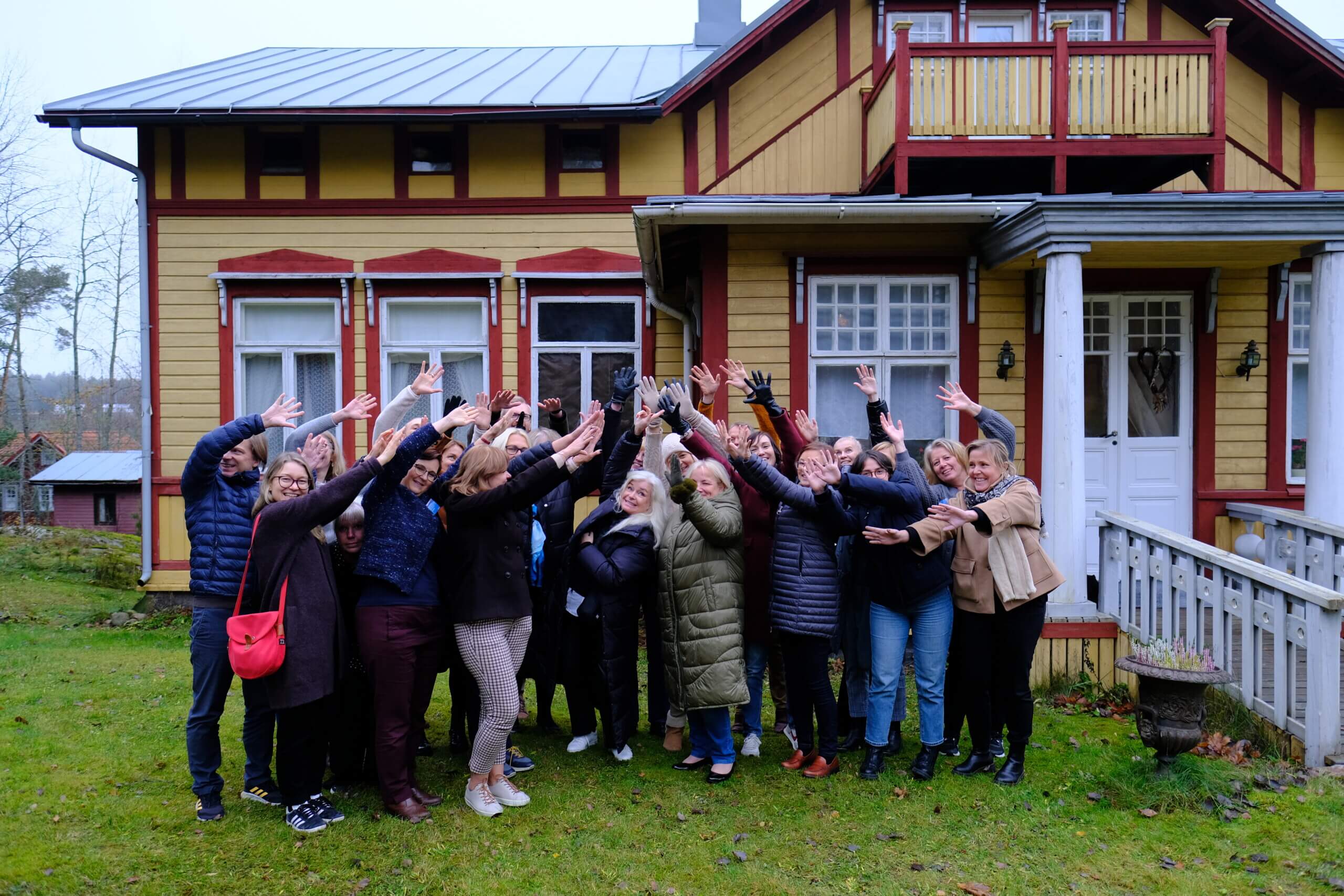 en grupp människor sträcker händerna upp i luften framför en gammal träbyggnad
