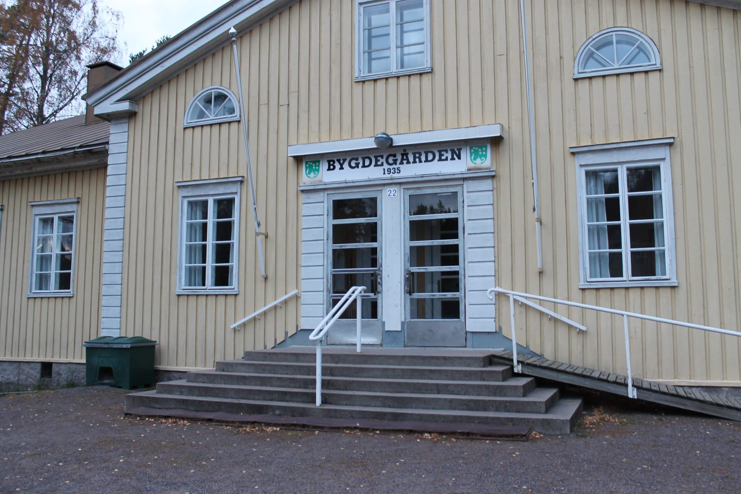 Bygdegården i Tenala fotograferat utifrån. huset är gult och en trappa som leder upp till ingngen där det finns dubbla dörrar med en skylt ovanför där det står "Bygdegården".