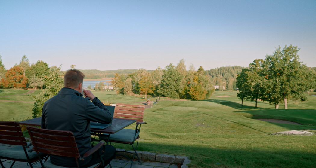 Man jobbar på bärbar dator på golfbana.