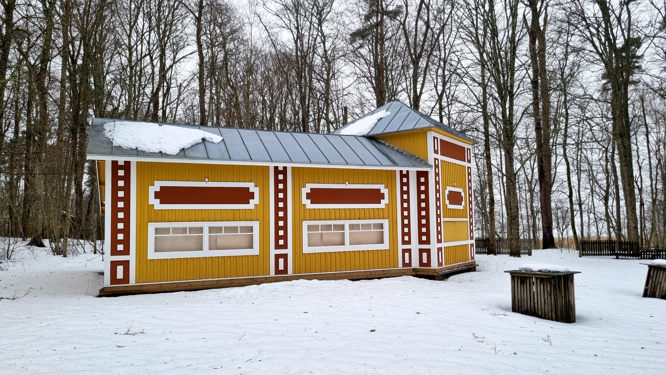 Gammaldags kiosk eller buffébyggnad bland snö och träd.