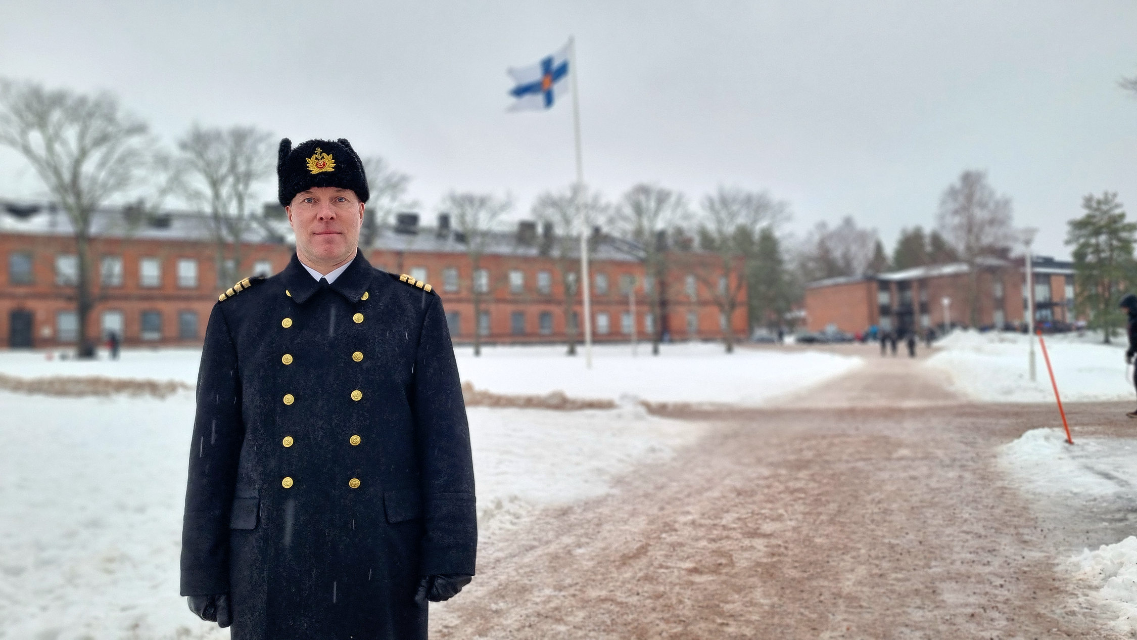 Brigadkommendör i uniform med flagga i bakgrunden.