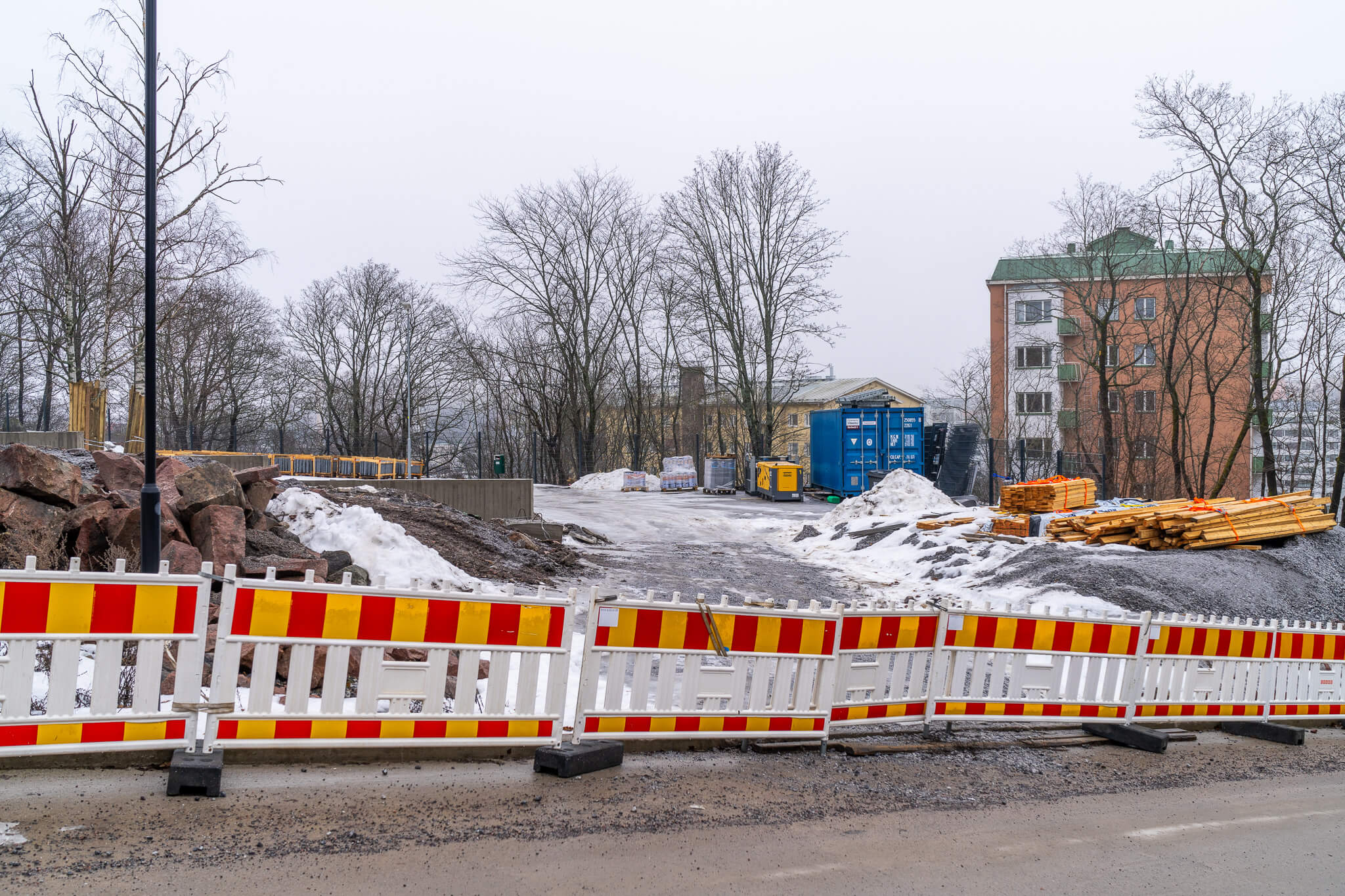 Delvis snötäckt byggarbetsplats och staket i vitt, gult och rött