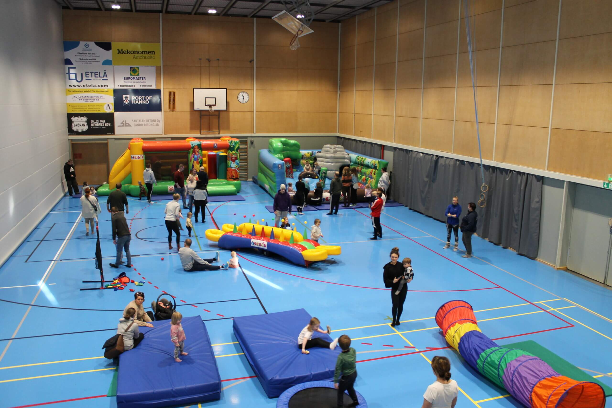 Barn och föräldrar inomhus i en gymnastiksal. Det är sportlov och i salen finns det färgglada hoppborgar, tunnlar och andra lek-stationer.