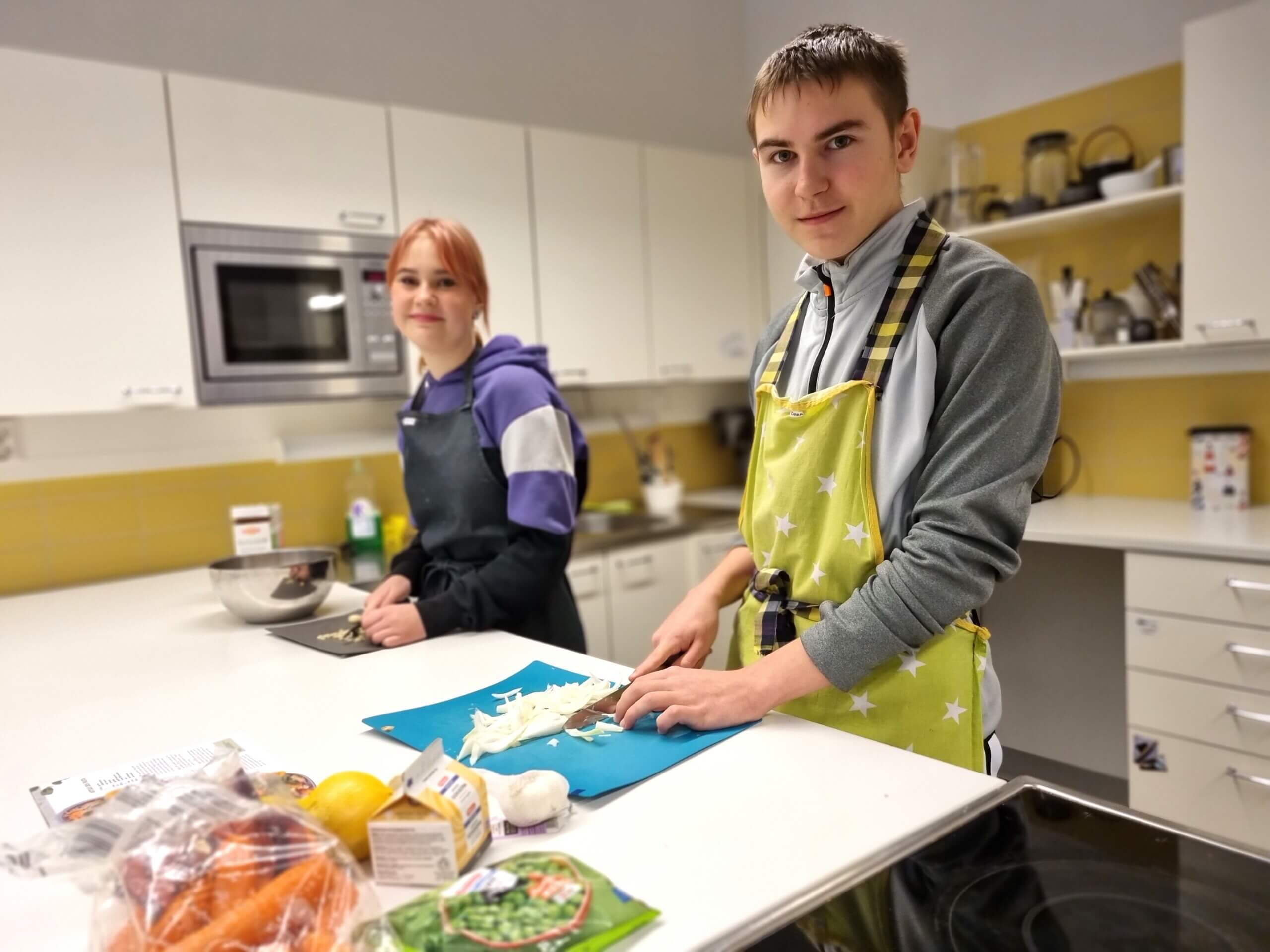 En flicka och en pojke som tillagar mat i skolkök.