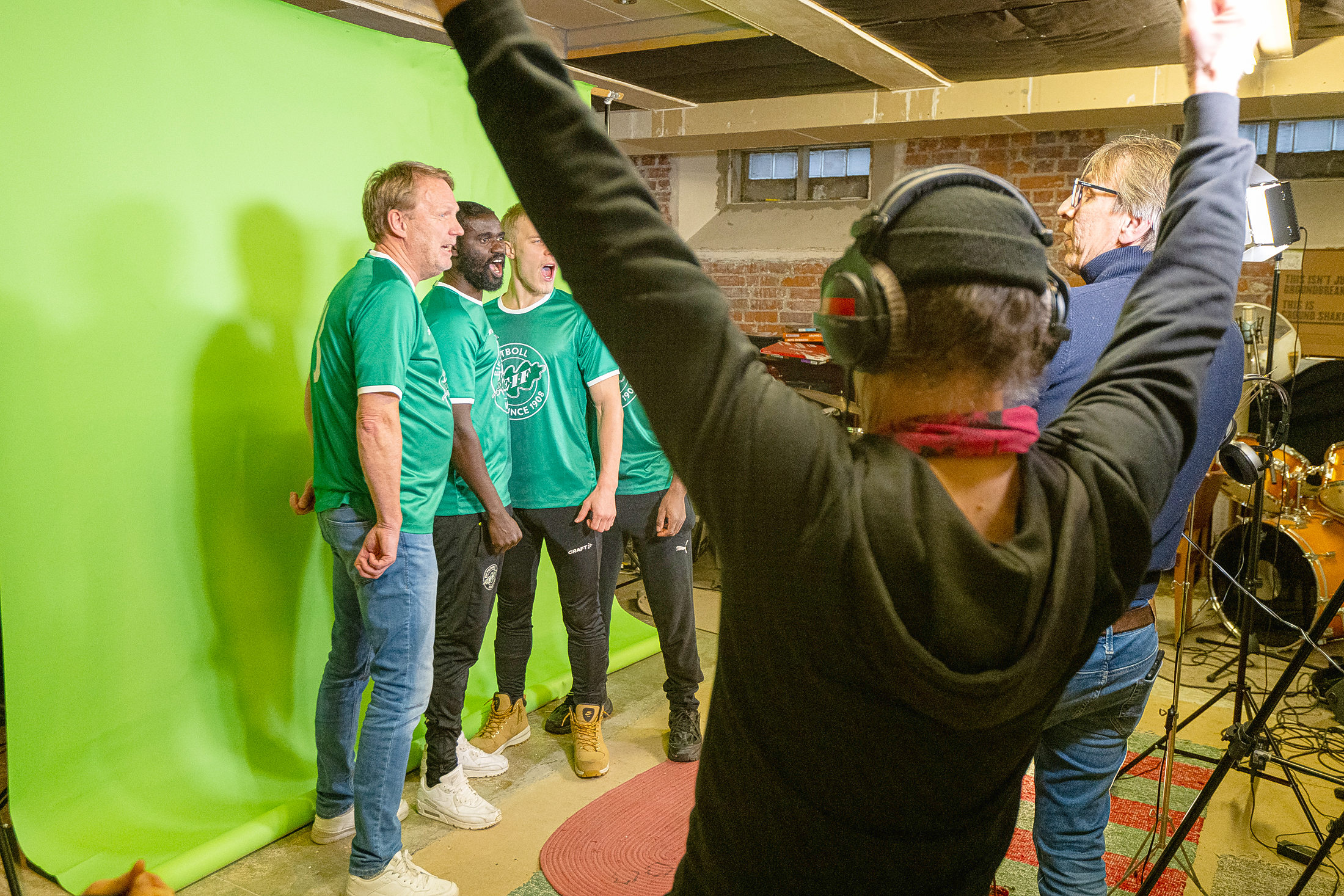 Män igröna fotbollströjor spelar in körsång i studio.