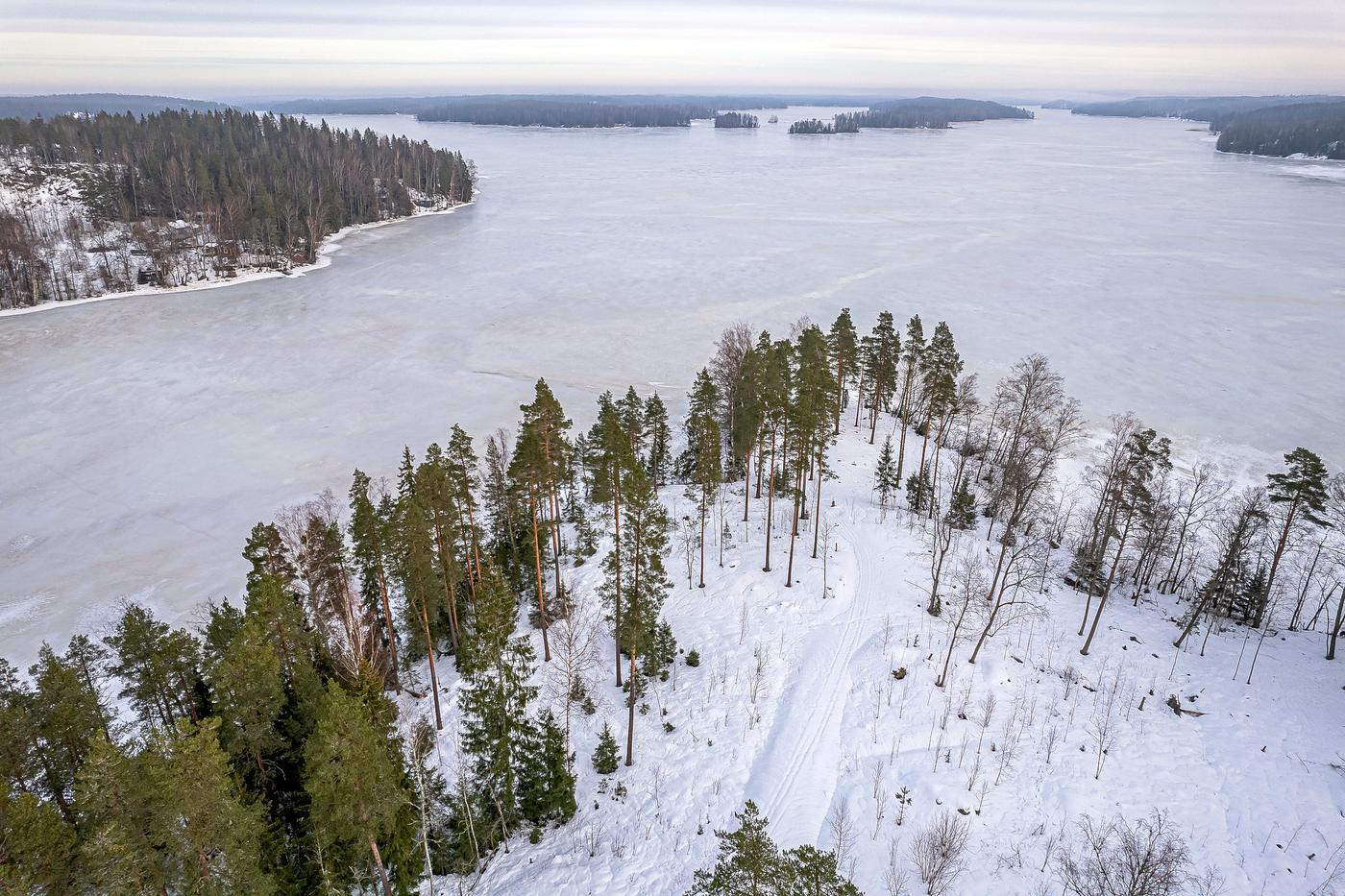 Flygbild av snötäckt udde vid sjö.