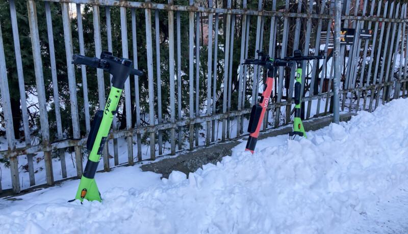 Tre sparkcyklar i grönt och rött som sticker upp ur en snöhög på en trottoar