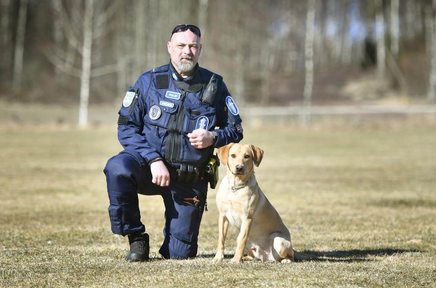 Polis på huk bredvid en hund med ljus päls