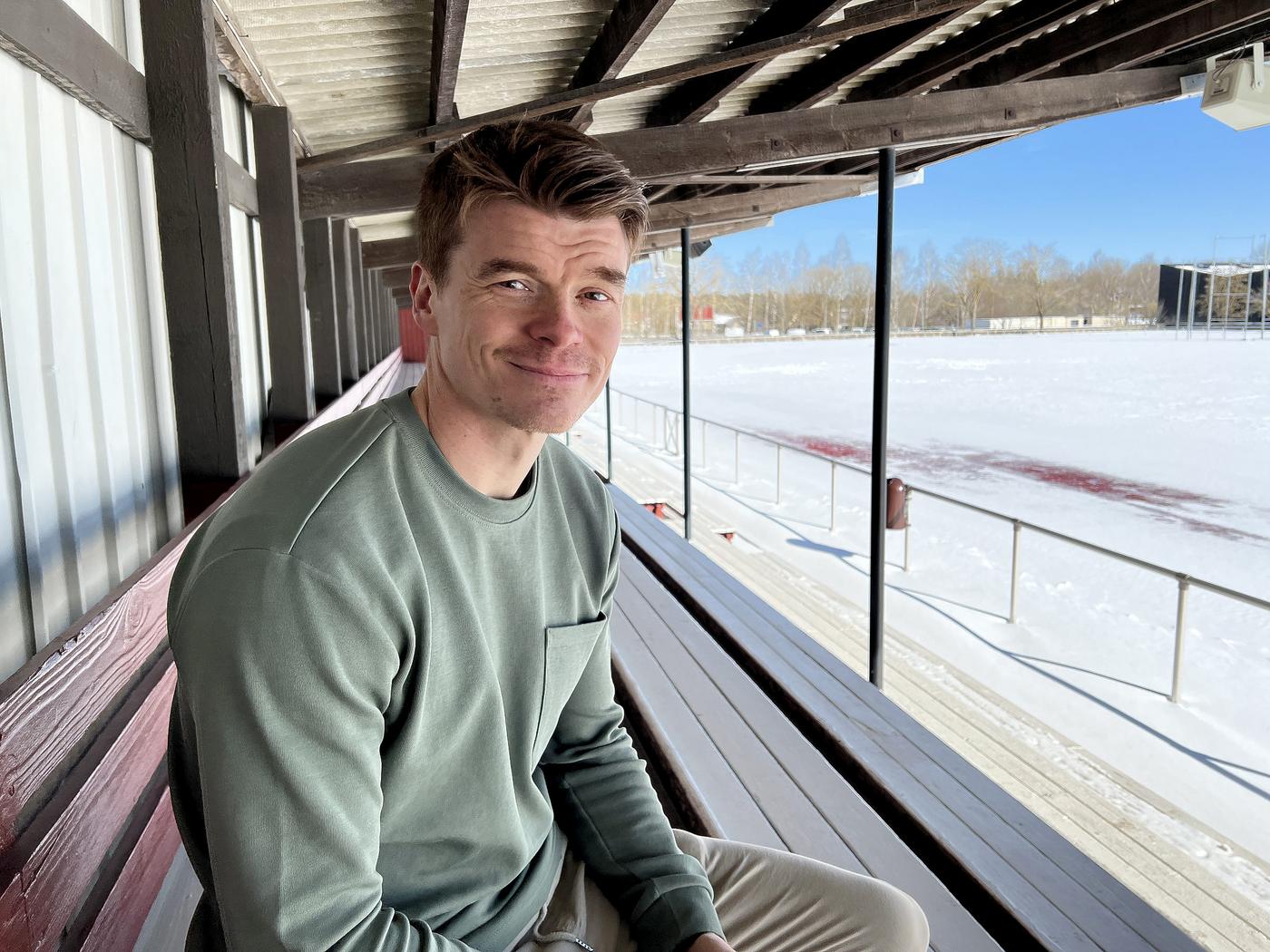en man sitter på en läktare vid en snötäckt fotbollsplan