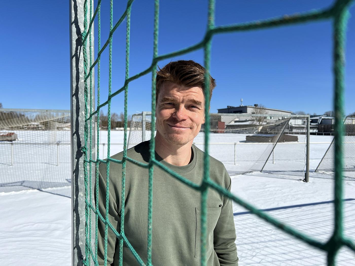 en man står bredvid ett fotbollsmål på en snötäckt fotbollsplan