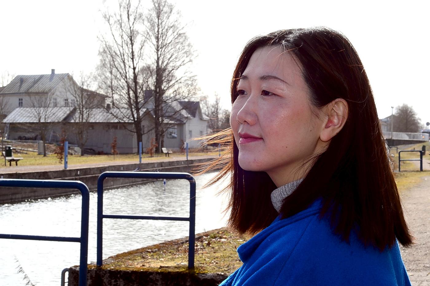 en kvinna i blå jacka sitter vid ett vattendrag