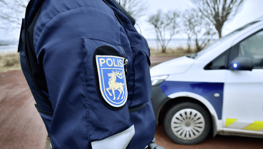 Närbild på person iklädd polisuniform, i bakgrunden står en polisbil