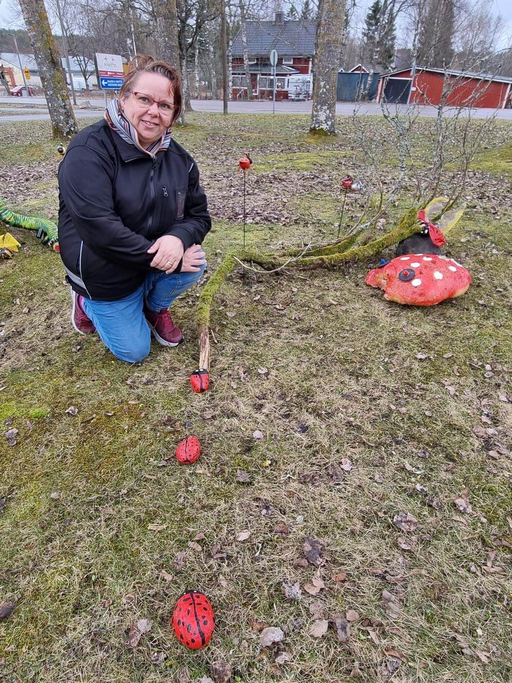 Kvinna som sitter ner på gräsmatta och placerar ut nyckelpigor gjorda av stenar.