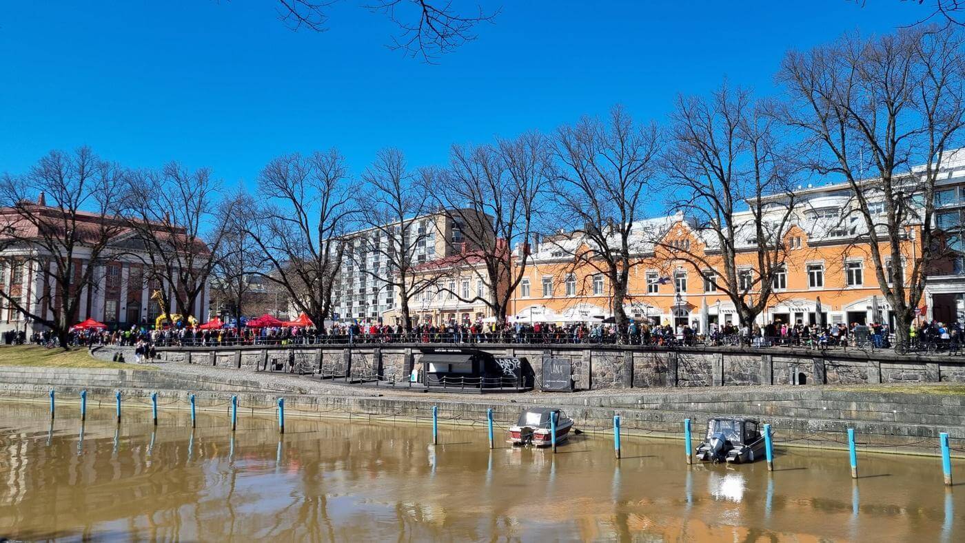 mängder av människor på ett torg en vårdag med en brun å i förgrunden