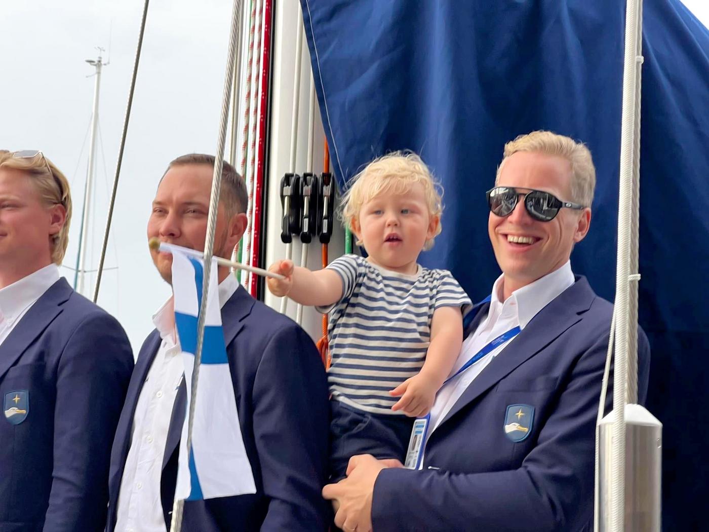 en man står med sitt barn i famnen på en segelbåt.