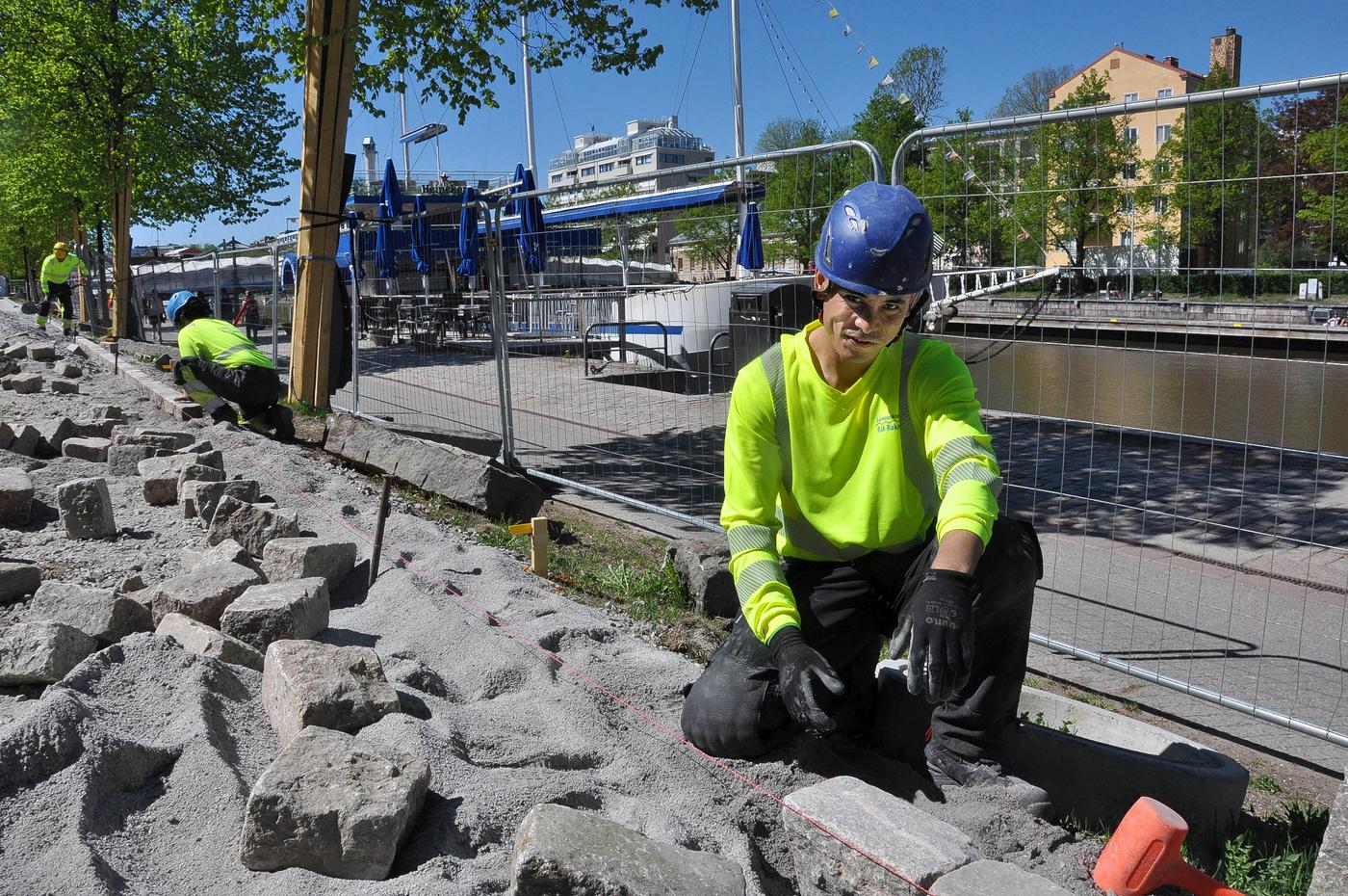 En man i blå hjälm och gul jacka lägger stenar på en cykelled.