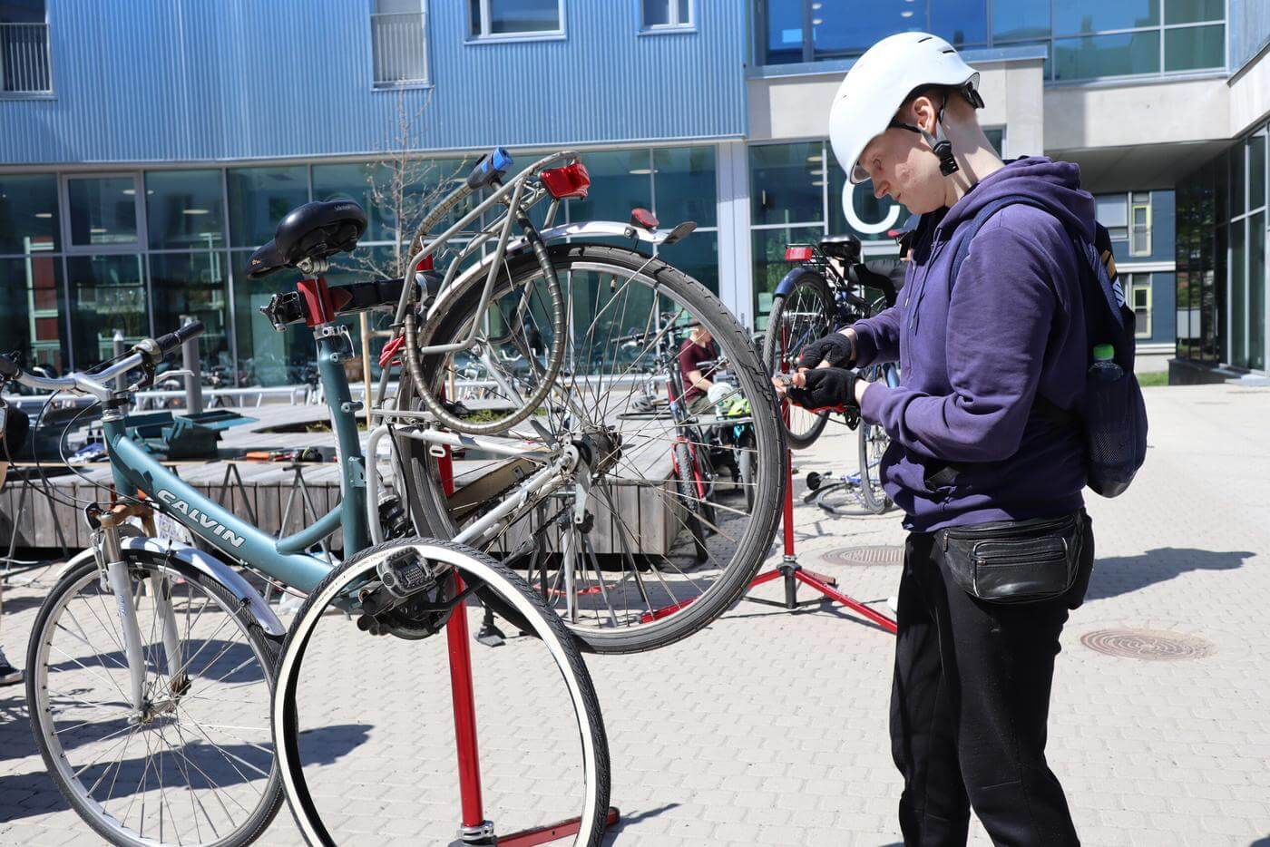 en person reparerar en cykel som fästs på en ställning. Personen har en vit cykelhjälm på huvudet.