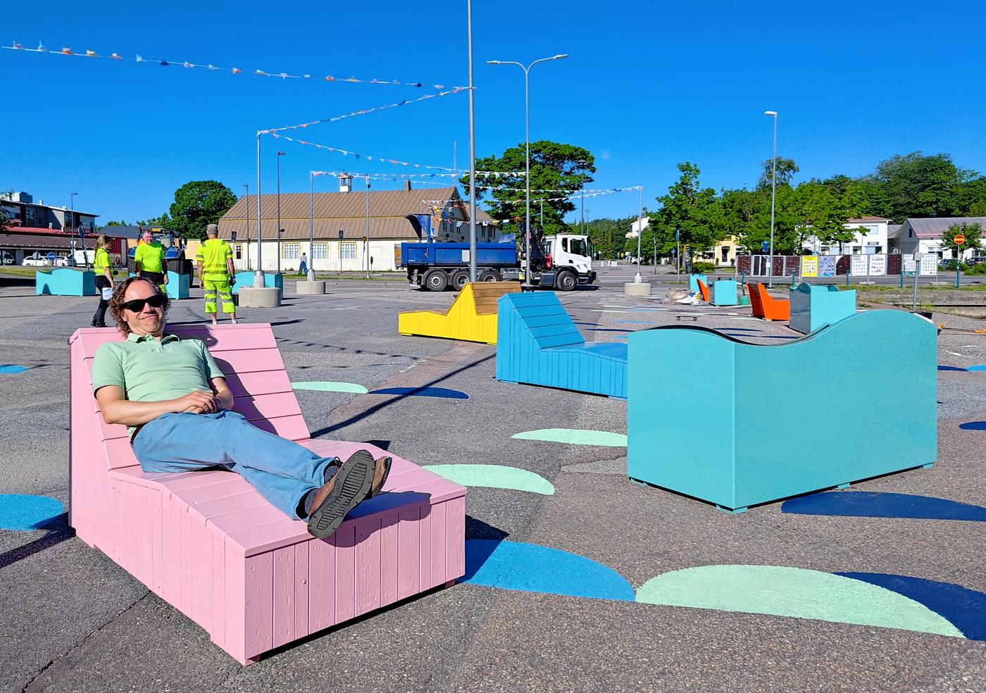 Man sitter på en rosa trädivan på ett färgglatt torg.