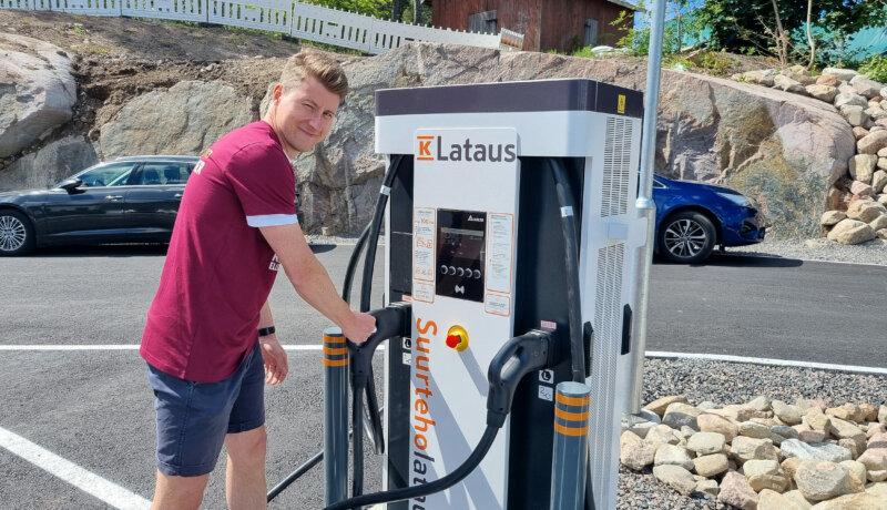 Man i t-skjorta och shorts visar upp en laddstation för elbilar.