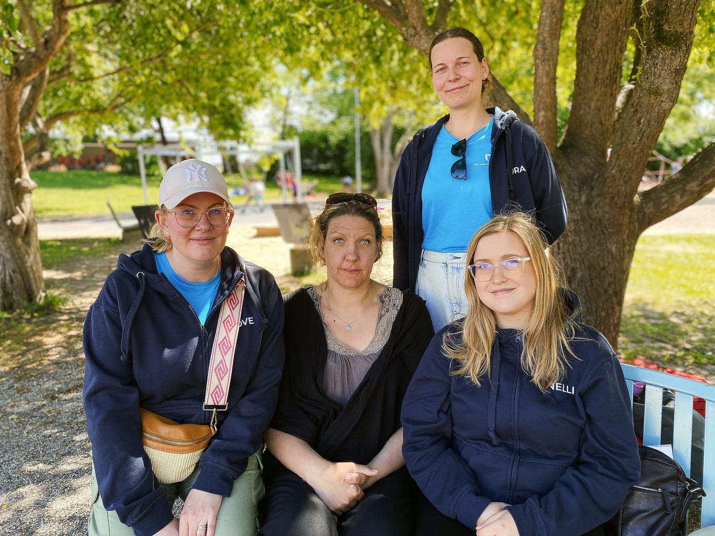 Fyra kvinnor sitter på en bänk i en park.