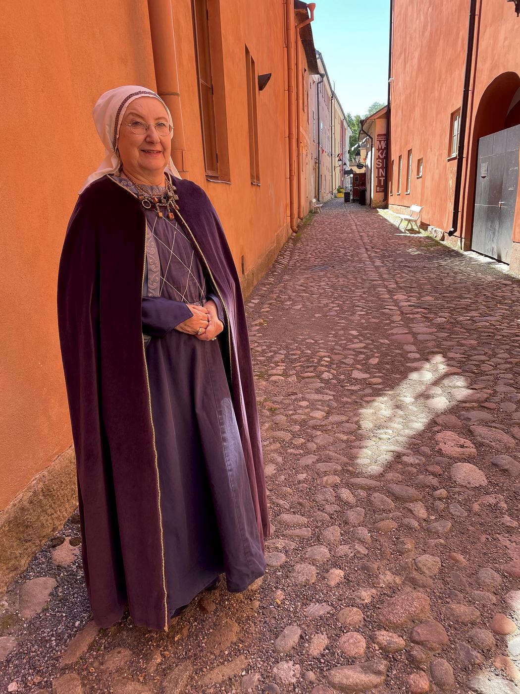 Sirpa Rinne i sin kostym som består av en ljuslila långklänning och en mörkare mantel.