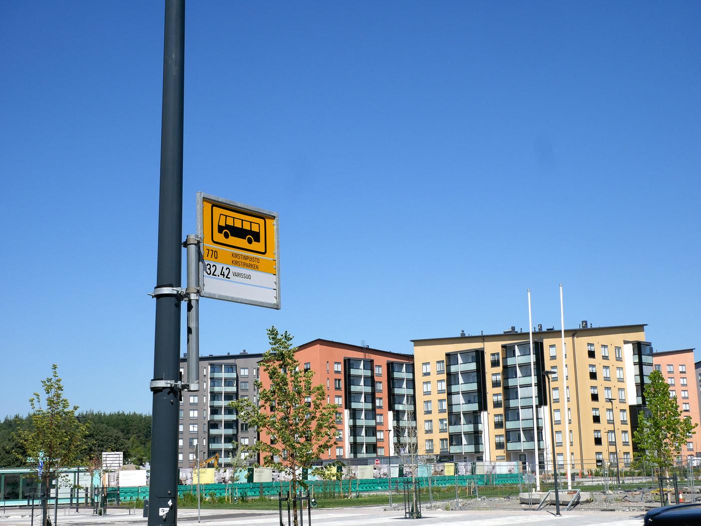 Busshållplats med höghus i bakgrunden.