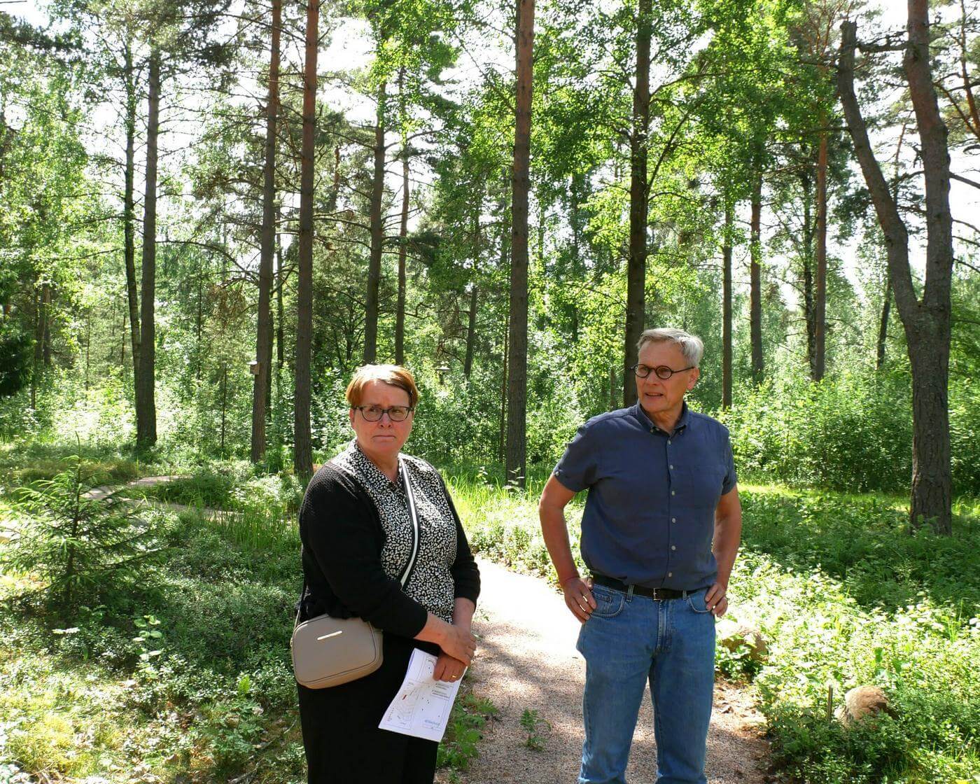 Två personer står vid skogsbegravningsfältet.