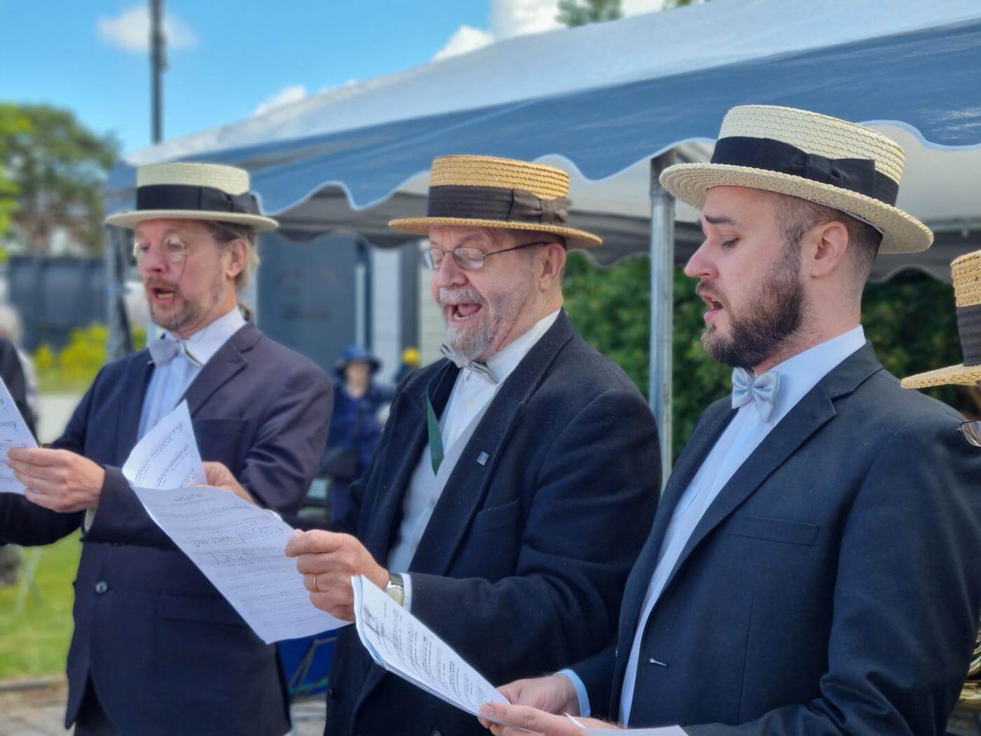 Tre män som sjunger iklädda kostymer och halmhattar.
