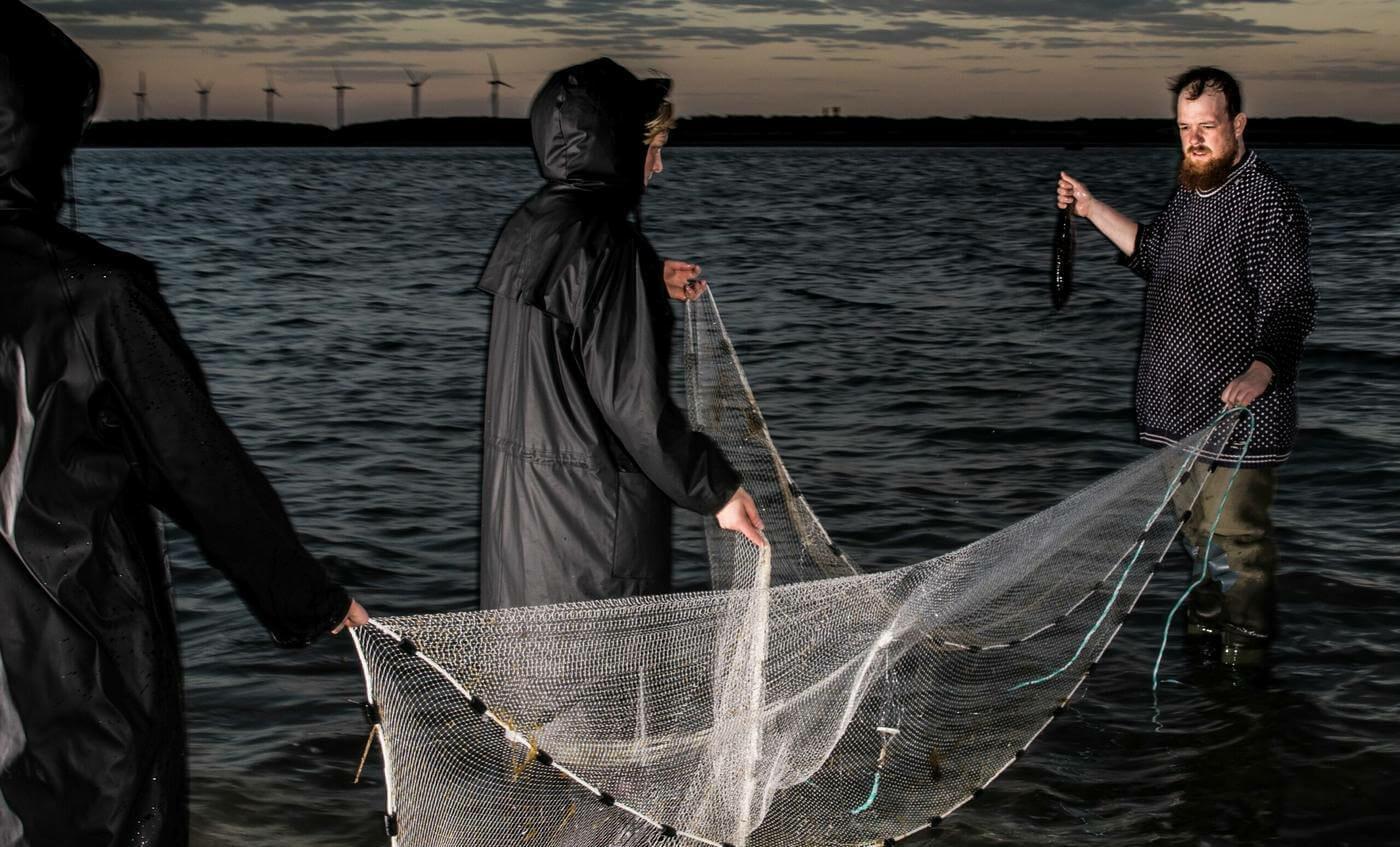 en bild på tre människor i vattnet med ett fiskenät