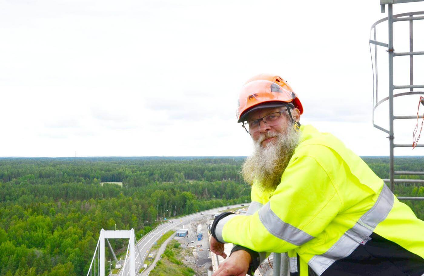 en skäggig man i hjälm och gul jacka tittar ner från en lyftkran