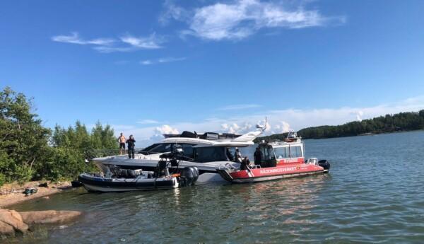 Stor motorbåt och två räddningsbåtar vid strand.