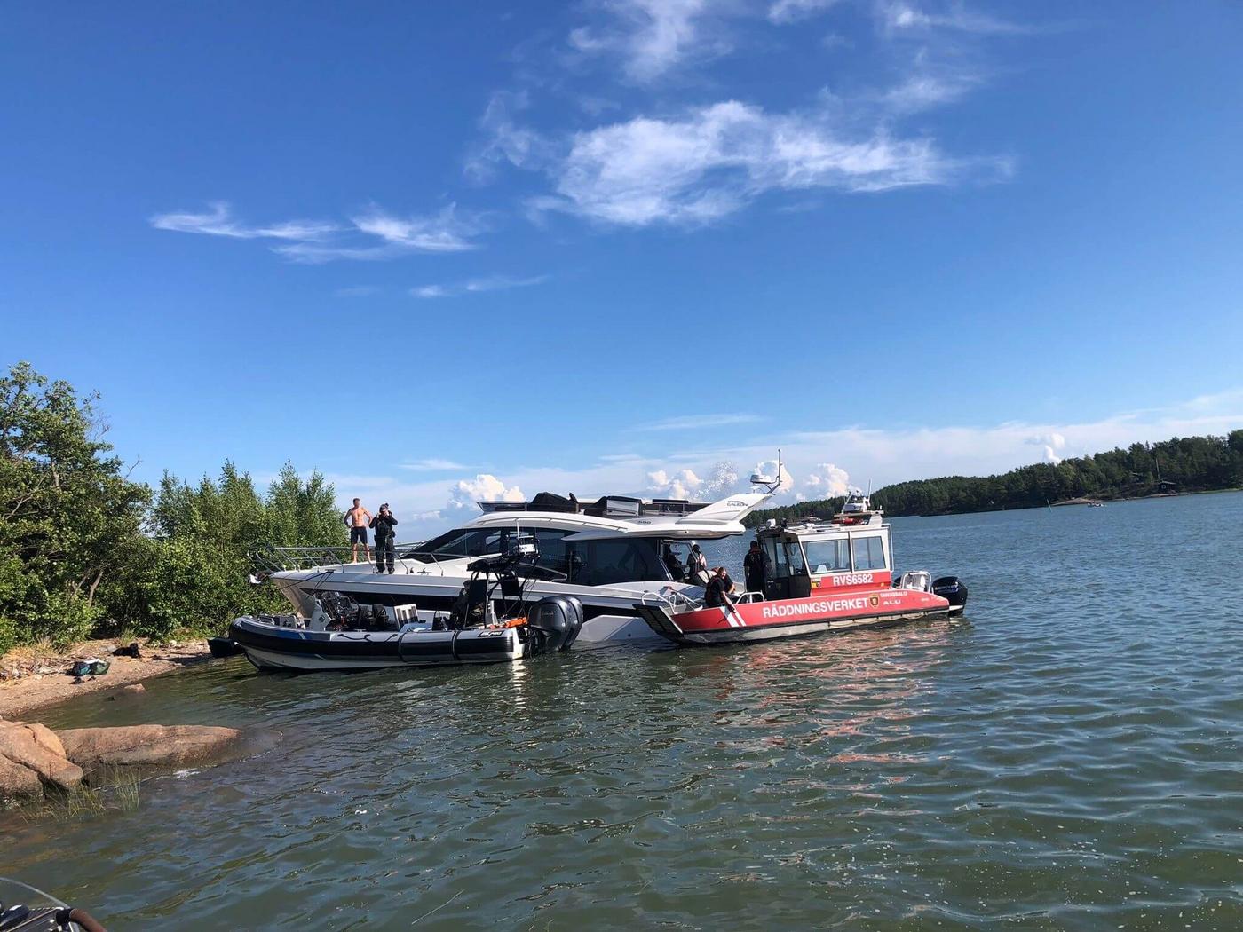 Stor motorbåt och två räddningsbåtar vid strand.