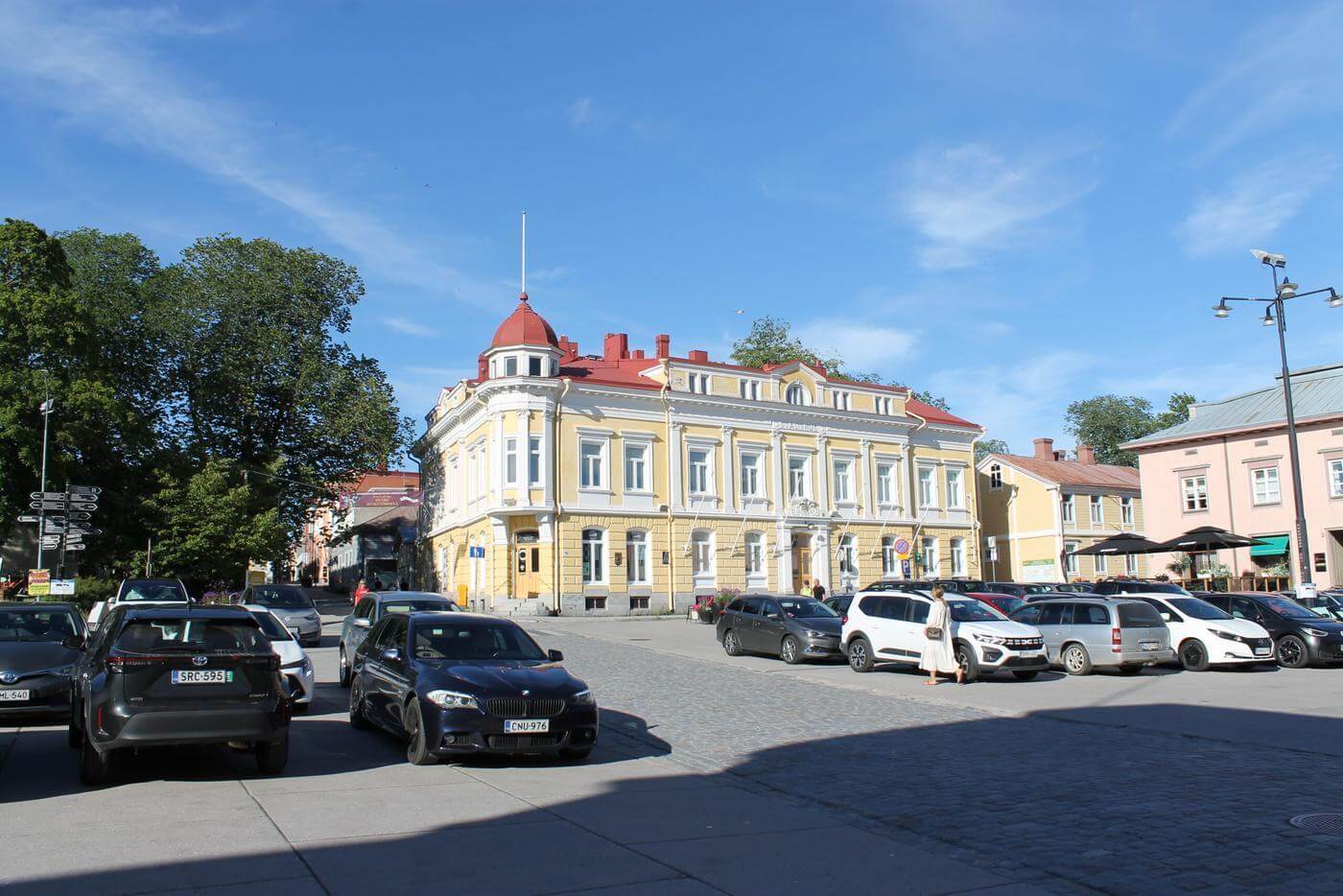 Bilar parkerade på Råhustorget i Ekenäs. I bakgrunden ser man ett gult stenhus och en gågata.