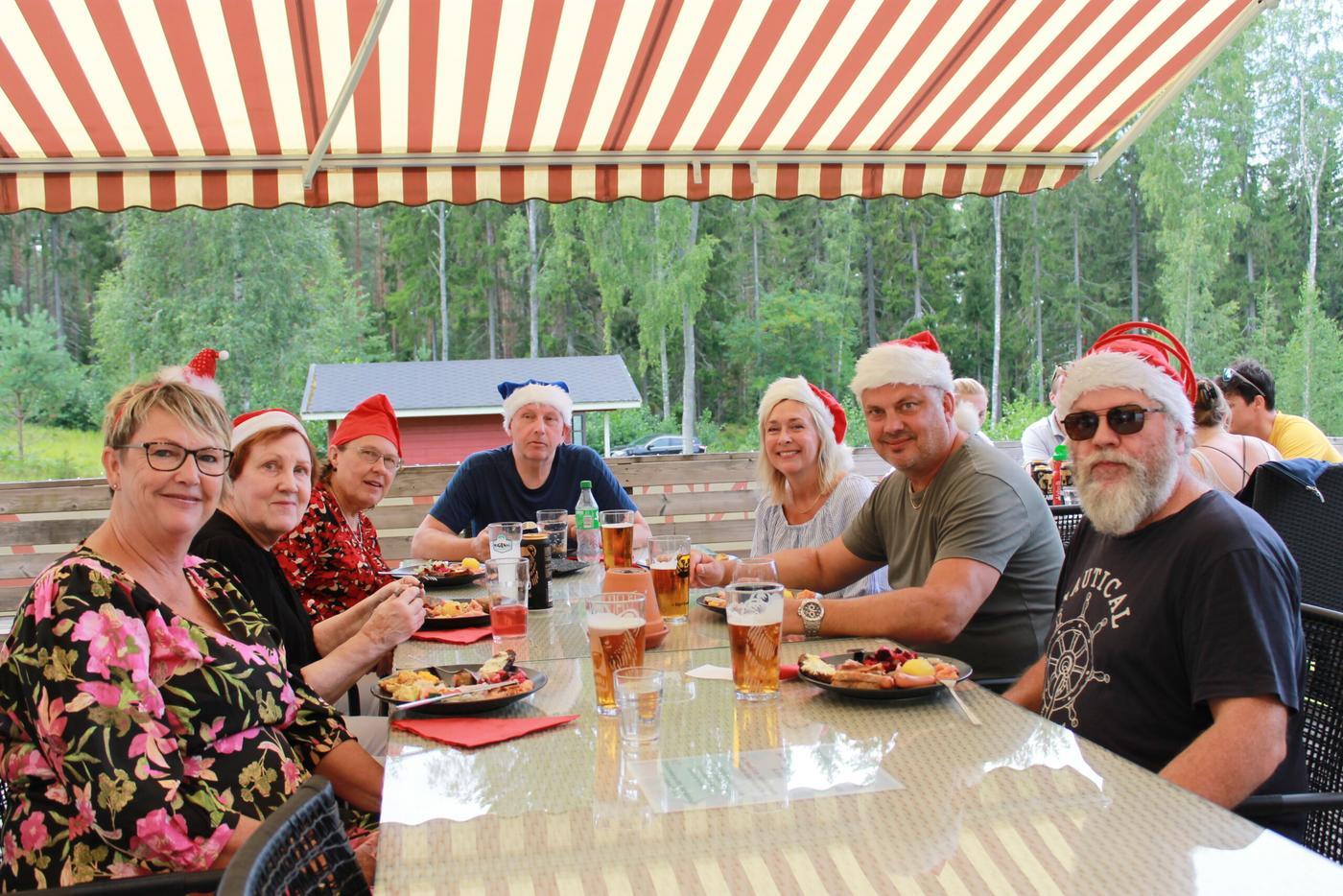 Ett större sällskap sitter samlat runt ett bord på restaurangen Skatafé i Bromarv. Skatafé har jul i juli och därför bär sällskapet tomteluvor.