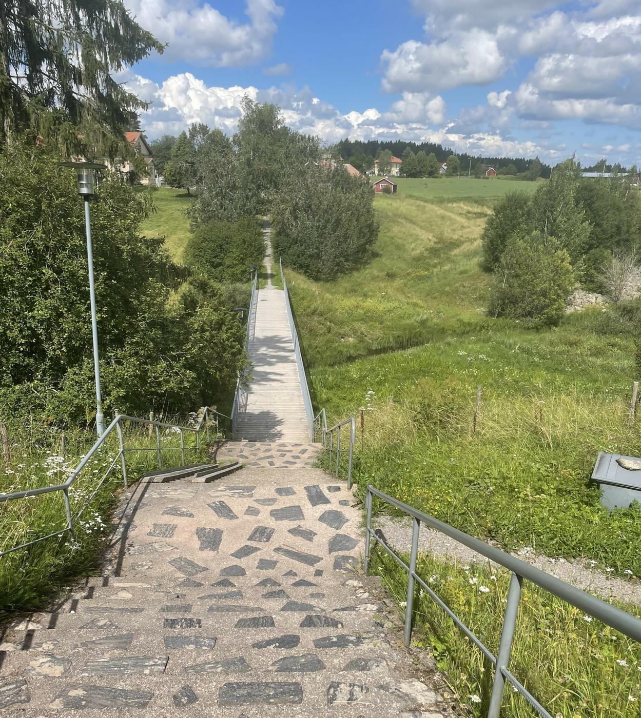 Bild på ett vackert grönt landskap med en bro och trappor i mitten. 