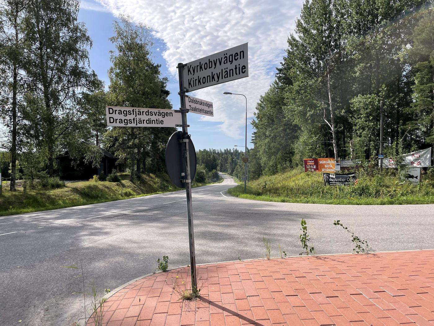 Avtag längs asfalterad väg. Vägskylt med vägarnas namn mitt i bilden.